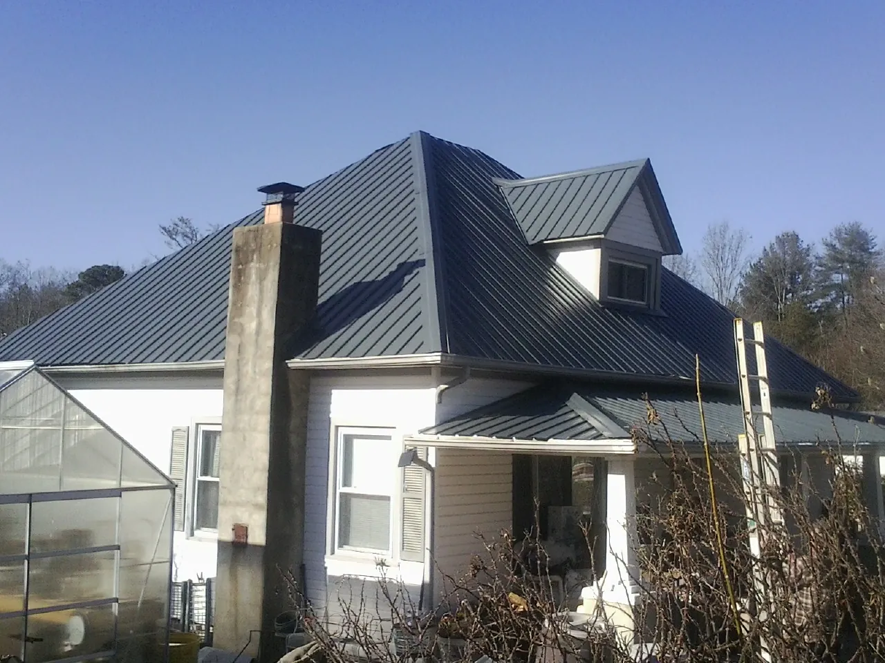 Dark blue standing seam metal roof on a white farmhouse with dormer — Slate & Tile Roof Repair by Roofing Brothers in Bayport