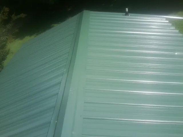 New green metal panels meeting at the ridge of a roof — Flat Roof Repair work by our crew in Bayport