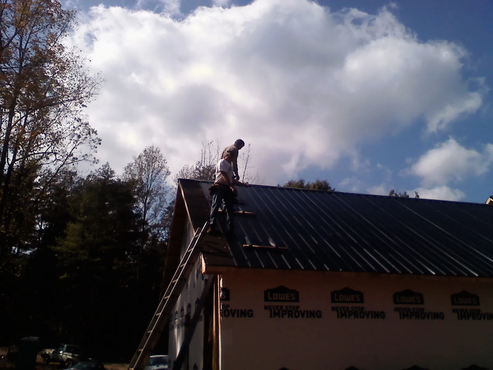 Roofer fastening dark metal panels high against a cloudy sky, from a Roof Inspection job in Bayport