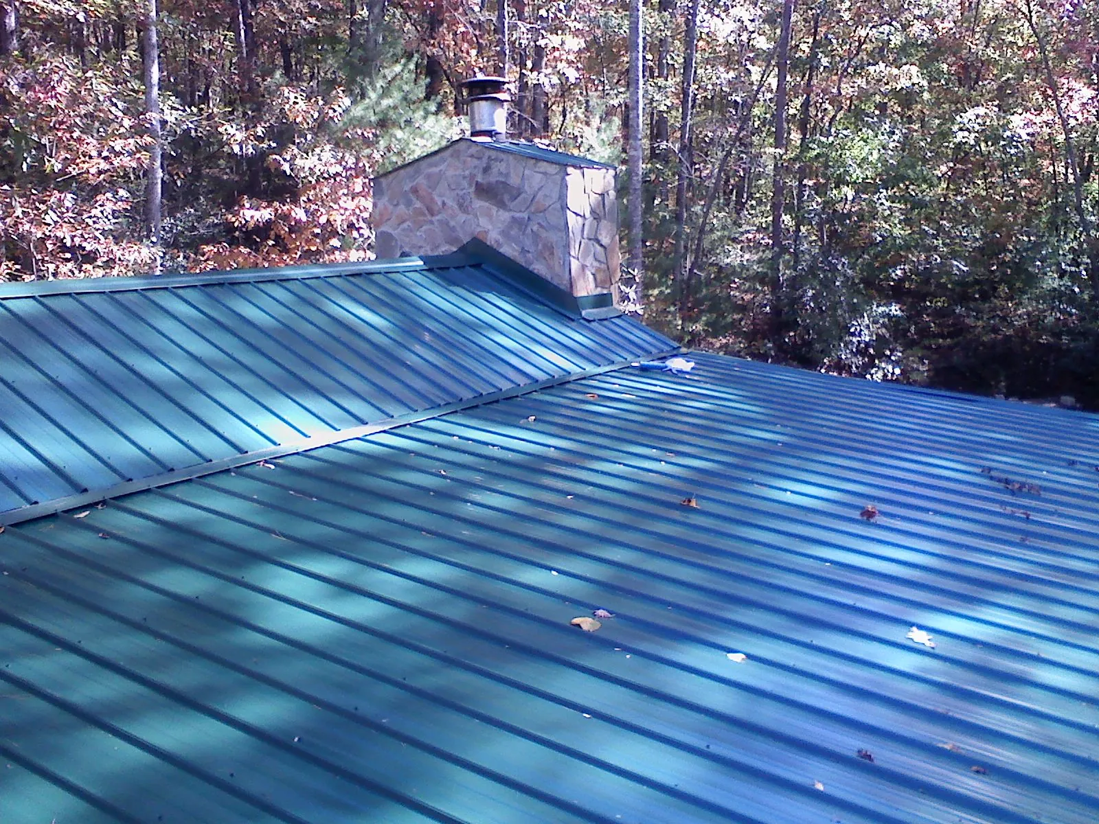 New green metal roof and stone chimney surrounded by autumn woods in Bayport