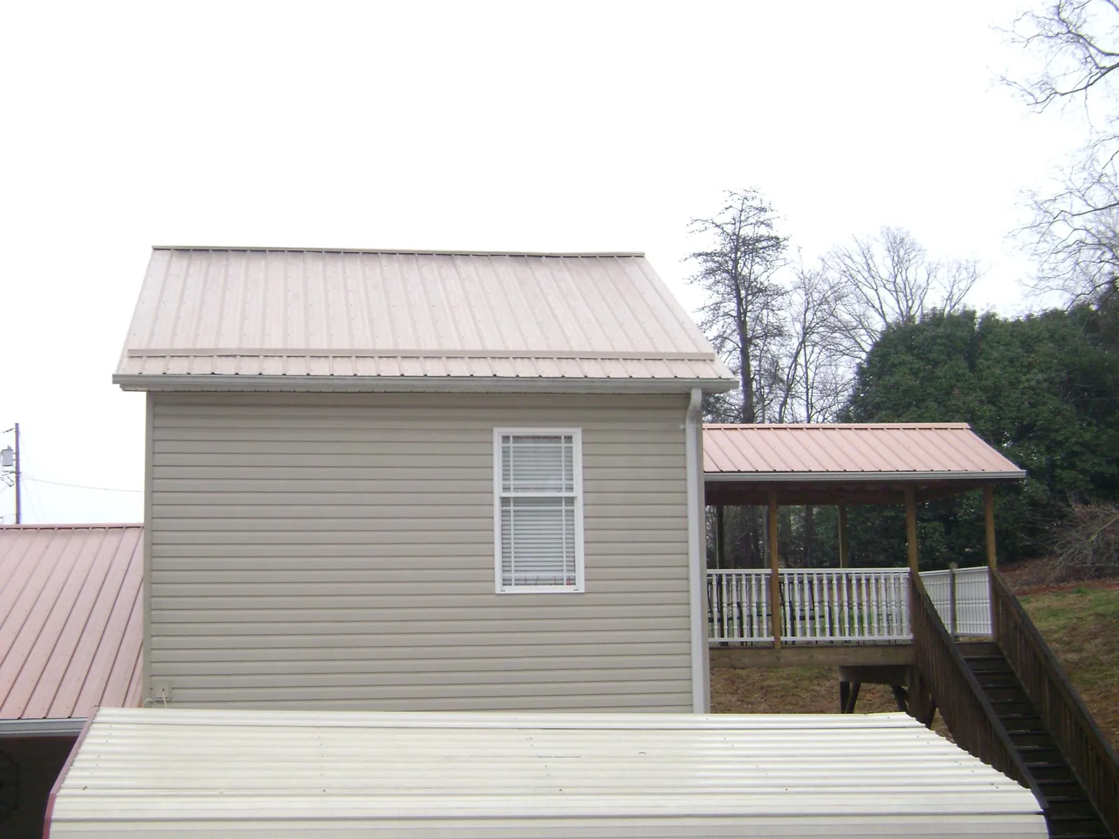Tan metal roofs on a two story addition and attached porch, from a Roof Replacement job in Bayport